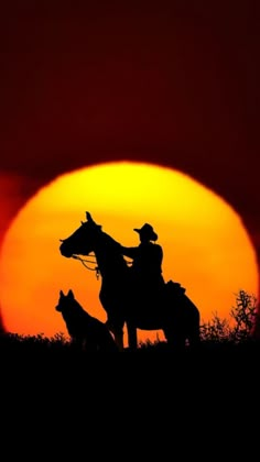 the silhouette of two cowboys on horseback in front of an orange sun