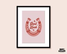 a framed poster with the words good luck in red and pink on it, against a beige background