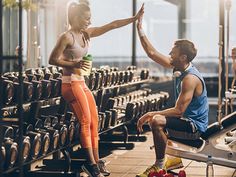 a man and woman sitting on exercise equipment in a gym, giving each other high fives