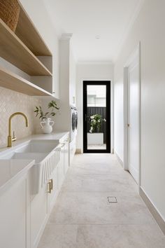 a long white kitchen with open shelving on the wall and sink in the center