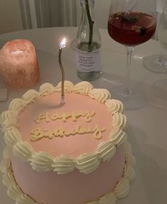 a pink birthday cake sitting on top of a table next to a glass of wine