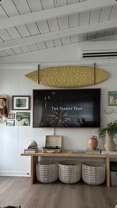 a surfboard is hanging on the wall above a table with baskets and vases