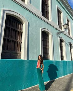 a woman standing in front of a blue building with shutters on the sides and windows