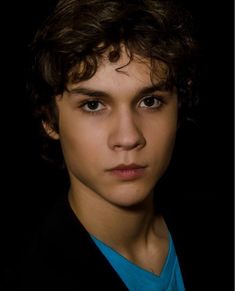 a young man with curly hair wearing a blue shirt and black blazer looking at the camera