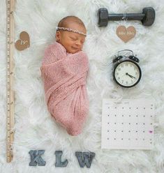 a newborn baby wrapped in a pink blanket next to a clock, ruler and other items