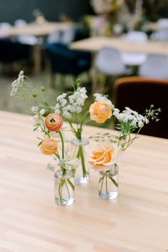 three glass vases with flowers in them sitting on a wooden table next to each other