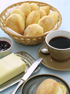 a table topped with plates of food next to cups of coffee and saucers on top of a blue table cloth