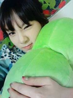 a woman laying on top of a bed with a green stuffed animal next to her