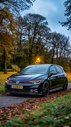 a black car parked on the side of a road next to some grass and trees