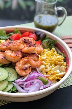 a bowl filled with shrimp and vegetables next to a glass of green liquid on a table