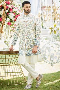 a man standing next to a table with flowers and chandelier hanging from it