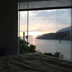 a bedroom with a large window looking out at the water and hills in the distance