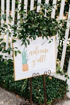 a welcome sign with a pineapple painted on it in front of a white picket fence