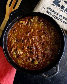 a black pan filled with chili next to a wooden spoon and fork on top of a table