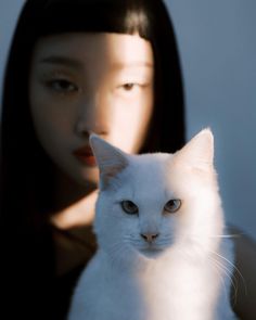 a white cat sitting on top of a woman's shoulder next to her face