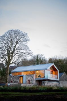 a stone house with a metal roof and glass windows on the front, surrounded by trees