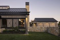 an exterior view of a modern home with stone walls and windows at dusk, showing the front entrance to the house