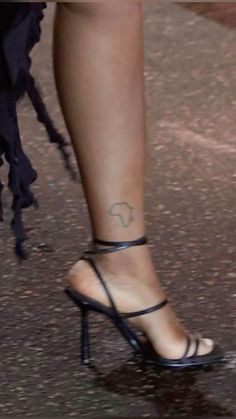 a woman's foot with a tattoo on her left ankle and black heels in the foreground