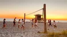 people playing volleyball on the beach at sunset