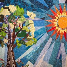 a quilted wall hanging with an image of a tree and sun in the background