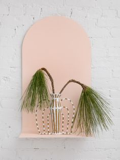 two plants are placed in a vase on a shelf next to a brick wall with a pink background