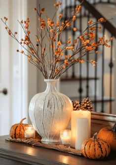 a white vase filled with lots of candles next to some pumpkins and flowers on a table