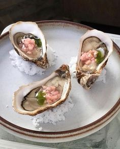 three oysters on a plate with white rice and garnished with pink flowers