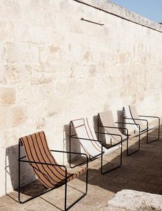 four chairs lined up against a wall on the side of a building with no one in it