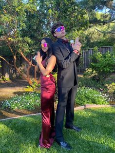 a man and woman in formal wear standing on the grass with their arms around each other