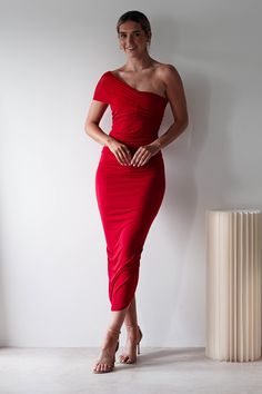 a woman in a red dress standing next to a tall white column with her hands on her hips