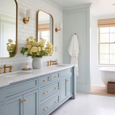 a bathroom with blue cabinets and white walls, two mirrors on the wall and flowers in a vase