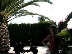 a girl standing next to a scooter and palm tree in the back yard