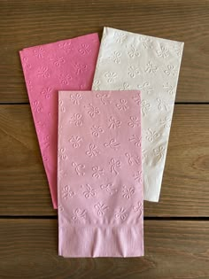 three pink and white napkins sitting on top of a wooden table