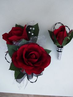 two red roses are sitting next to each other on a table with silver and black ribbons