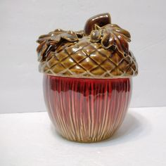 a red and gold vase with an apple on it's top sitting on a white surface