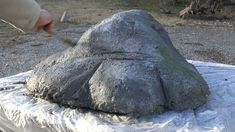 a person is using a knife to cut into a large stone object on a sheet of plastic