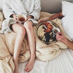 two people sitting on a bed with coffee and croissants in their hands