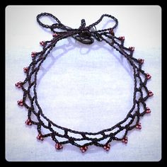 a close up of a necklace on a white surface with red beads and a black cord