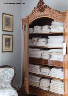 an old wooden bookcase filled with lots of papers next to a chair and pictures on the wall