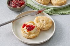 two small biscuits with jam on them are sitting on a plate next to a bowl of jelly