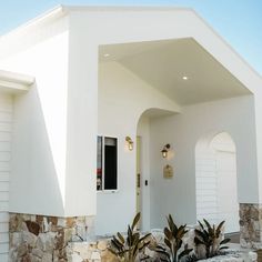 a white house with two plants in the front yard and an open door on one side