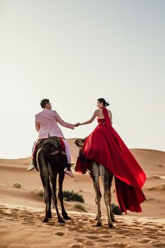 a man and woman riding on the back of a camel in the desert, holding hands