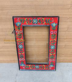 a red frame with flowers and leaves painted on the outside, sitting against a wooden wall