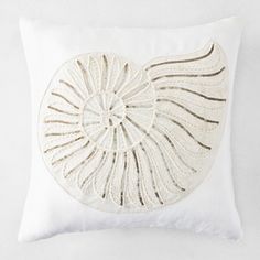 a white pillow with an embroidered shell on it's back and gold threadwork in the middle