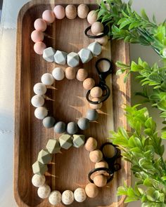 a wooden tray topped with lots of different types of beads next to a potted plant