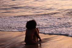 a woman sitting on the beach at sunset