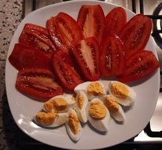 sliced tomatoes and hard boiled eggs on a white plate next to an oven burner