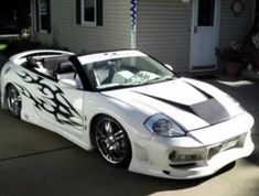 a white sports car with flames painted on it's hood parked in front of a house