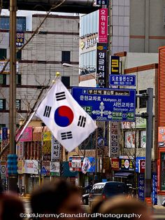 a korean flag is flying in the air on a city street with buildings and signs