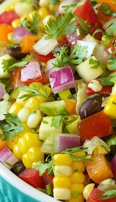 a bowl filled with corn and vegetables on top of a blue table cloth next to a fork